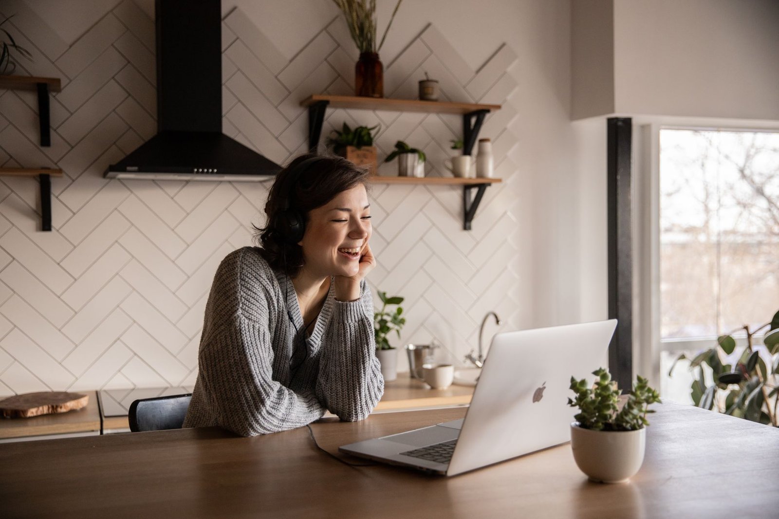 Smiling woman chatting on a laptop video call at her kitchen table