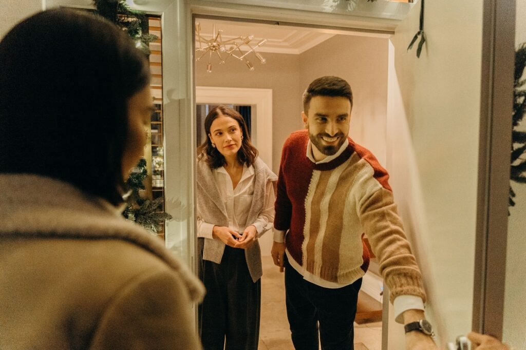 A couple smiling and greeting a guest at their sunlit front door