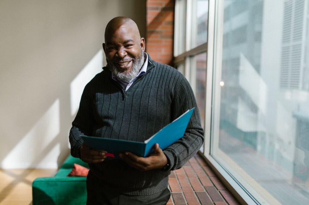 Cheerful man holding a folder, smiling warmly in a sunlit office