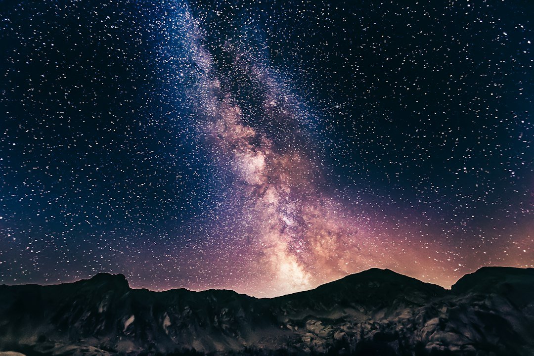 The Milky Way stretching across a starry night sky above dark mountains