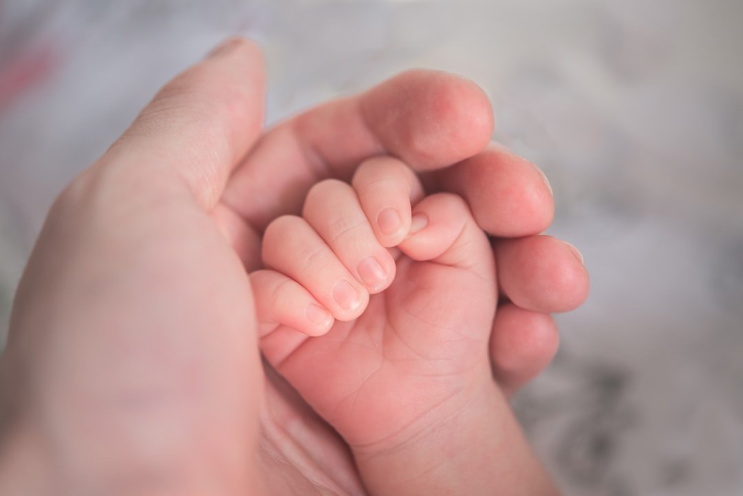 Close-up of a parent's hand holding a newborn baby's tiny hand