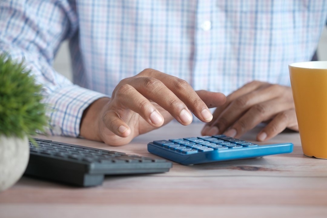Hand using a calculator while reviewing household finances at a desk