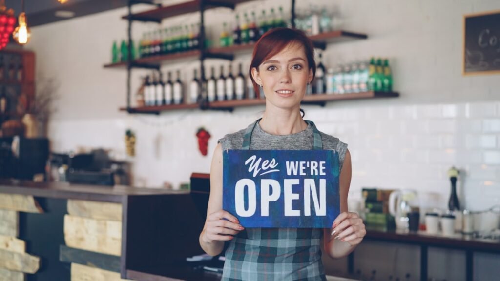 Confident woman small business owner holding open sign in her shop