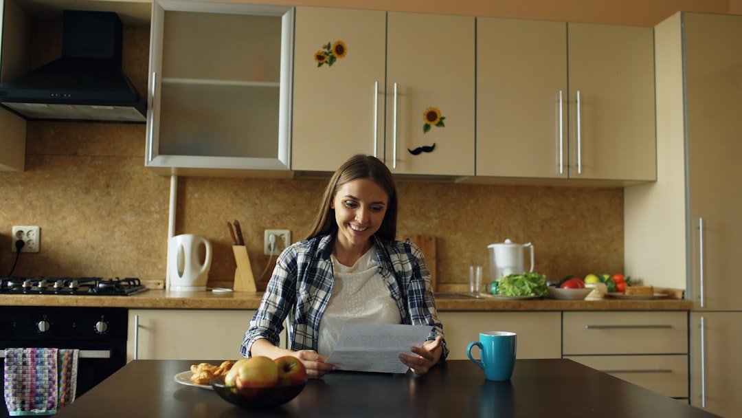 Woman smiling while reading at a sunlit kitchen table in the morning