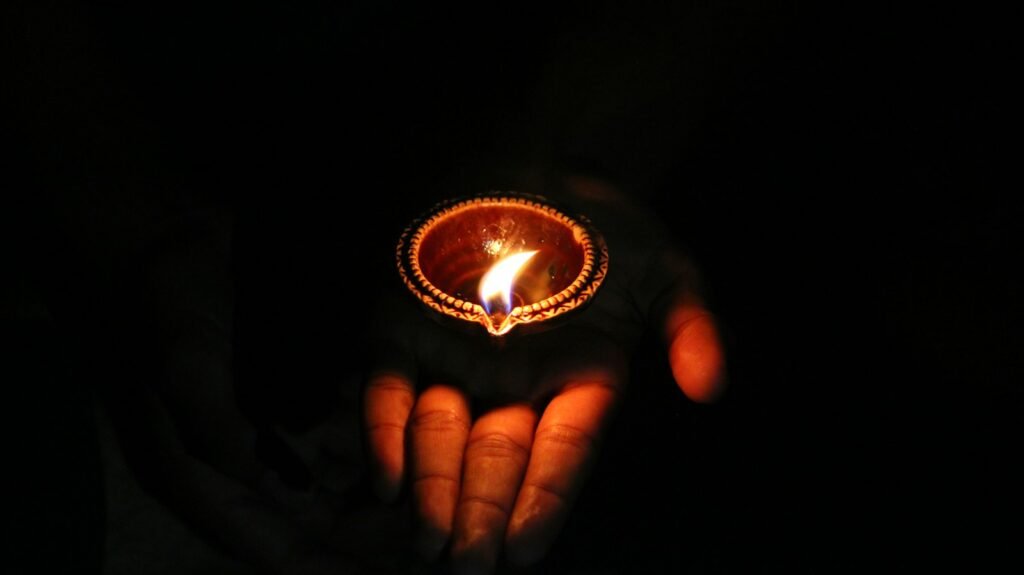 Hand holding a lit diya oil lamp during a puja ritual
