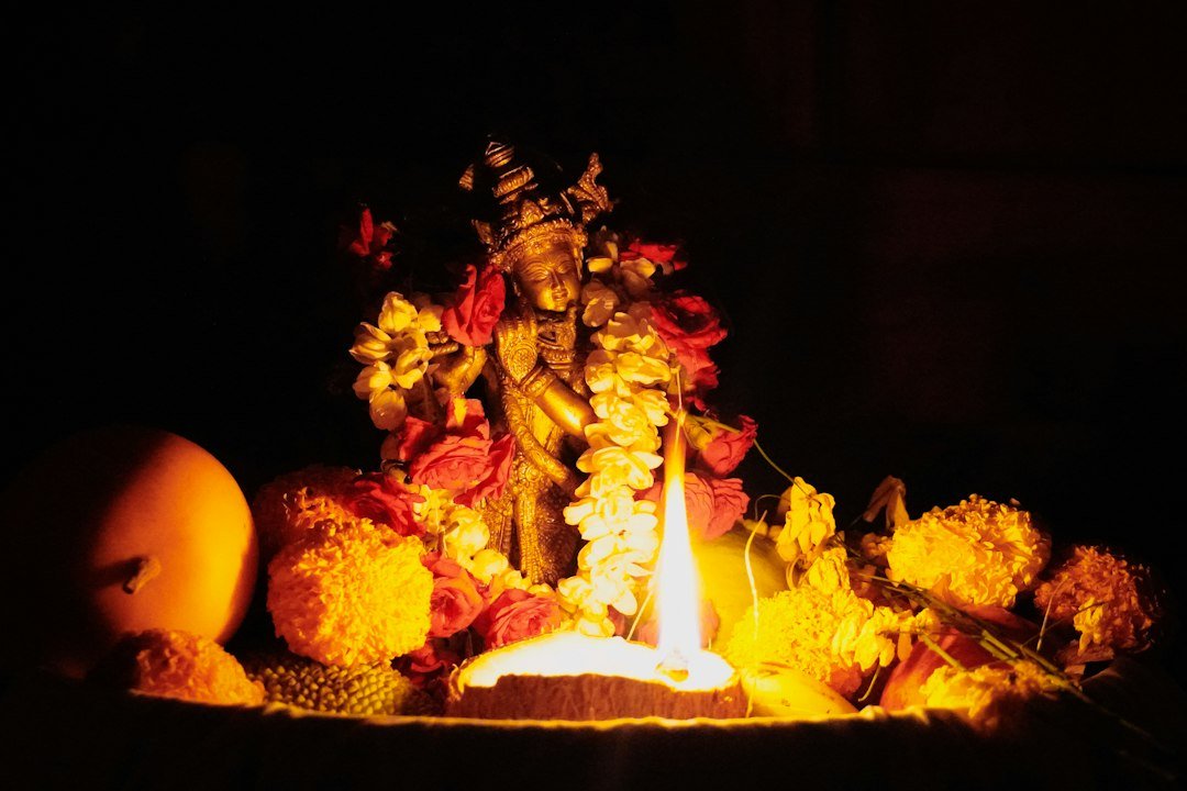 Deity statue adorned with flowers and a lit oil lamp