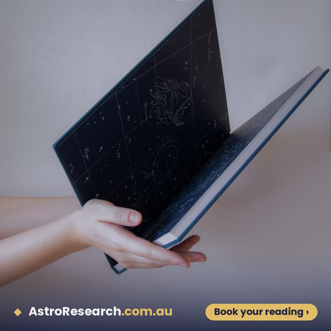 Hands holding an open book of star maps for a basic horoscope reading