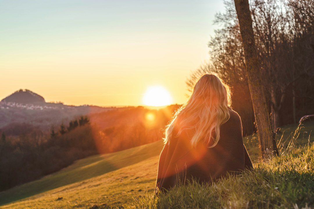 Woman sitting on a grassy hill watching a golden sunrise, the Sun's place in the sky that Vedic and Western astrology measure differently